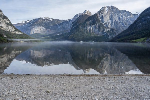 Quiet gravel lakeshore looking across Lake Hallstatt to alpine mountains